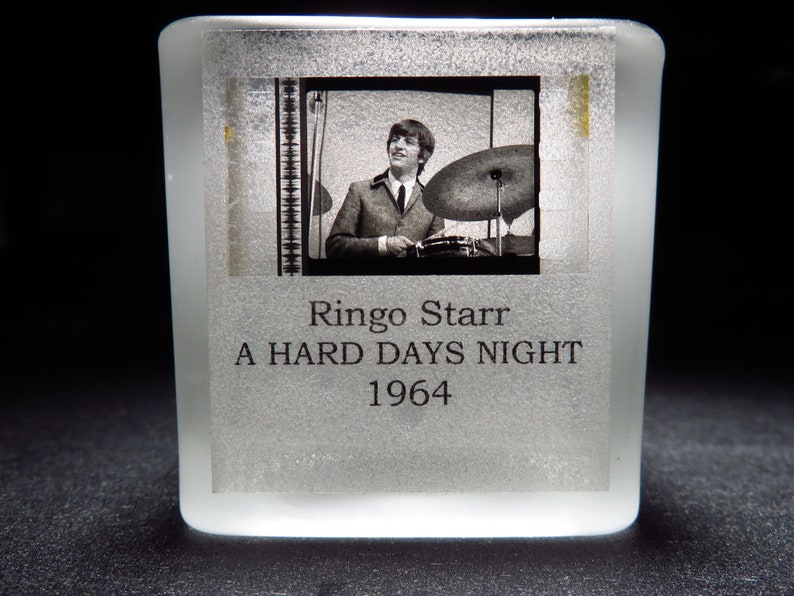 Op de afbeelding: Een zwart-witfoto van Ringo Starr die drums speelt, met de tekst "Ringo Starr A HARD DAYS NIGHT 1964" onder de foto.