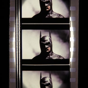 Puede incluir: Un traje de Batman negro y gris con una capucha puntiaguda y un fondo oscuro. El traje se ve en tres fotogramas diferentes de una película.