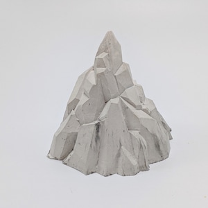 Pode incluir: Uma escultura geométrica de concreto branco que se assemelha a um pico de montanha. A escultura tem uma superfície áspera e texturizada e um topo pontiagudo.