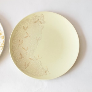 May include: A pale yellow ceramic dinner plate with a gold floral design. The design is concentrated on the left side of the plate.