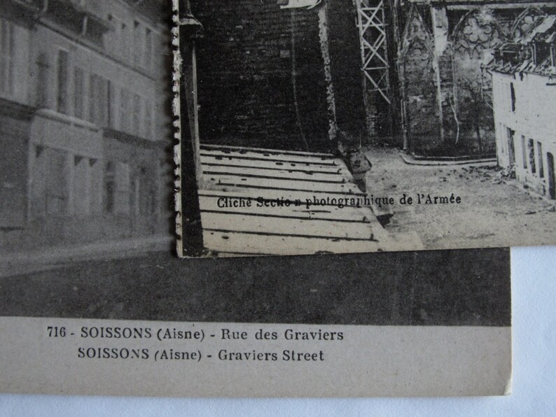 May include: Black and white photographic postcard of a street scene in Soissons, France. The text on the postcard reads "Clich&eacute; Section photographique de l'Arm&eacute;e 716 - SOISSONS (Aisne) - Rue des Graviers SOISSONS (Aisne) - Graviers Street"