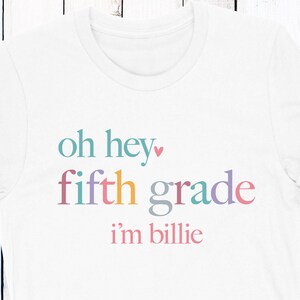 May include: White t-shirt with the text "oh hey fifth grade i'm billie" in rainbow colors.