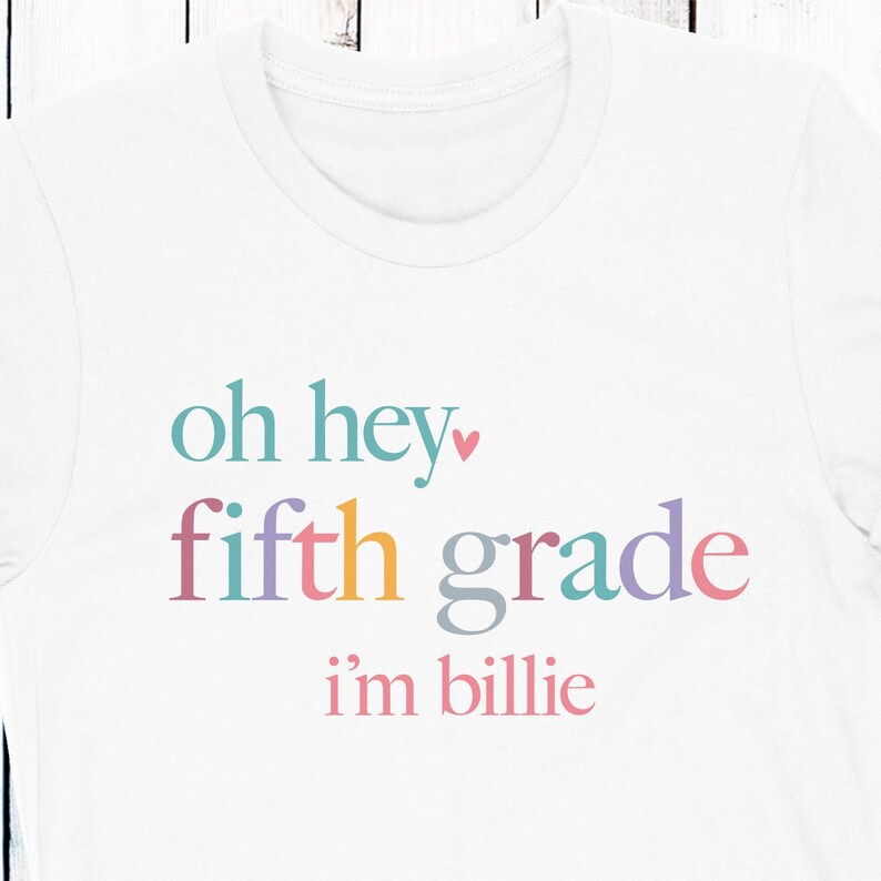 May include: White t-shirt with the text "oh hey fifth grade i'm billie" in rainbow colors.