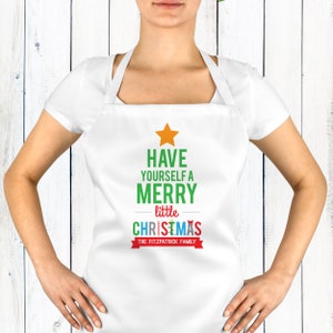 May include: White apron featuring a Christmas tree design. The tree is made of colourful letters that say "Have Yourself a Merry little Christmas" and a red ribbon with the text "The Fitzpatrick Family".