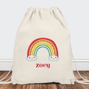 May include: A white drawstring bag with a colorful rainbow and two clouds with smiley faces. The name "zoey" is printed in red below the rainbow.