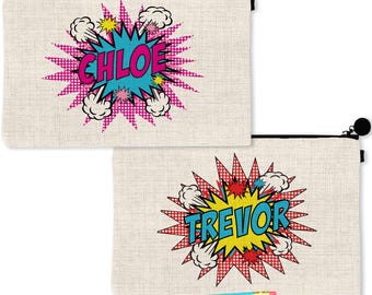 May include: Two rectangular beige canvas zipper pouches featuring comic book style graphics. One pouch displays the name CHLOE in pink letters inside a blue starburst, while the other shows TREVOR in blue letters inside a yellow starburst.