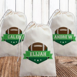 May include: Three white drawstring bags with green and brown football designs. The bags are personalized with the names "Caleb", "Elijah", and "Andrew".