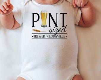 May include: White baby onesie with black text that reads "Pint sized - Brewed in Louisville" with a graphic of a beer glass and a wheat stalk.