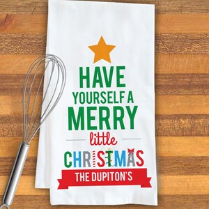 May include: White kitchen towel with a green Christmas tree design. The tree is made up of the words "Have Yourself a Merry little Christmas". The text "The Dupiton's" is in a red banner at the bottom of the tree.