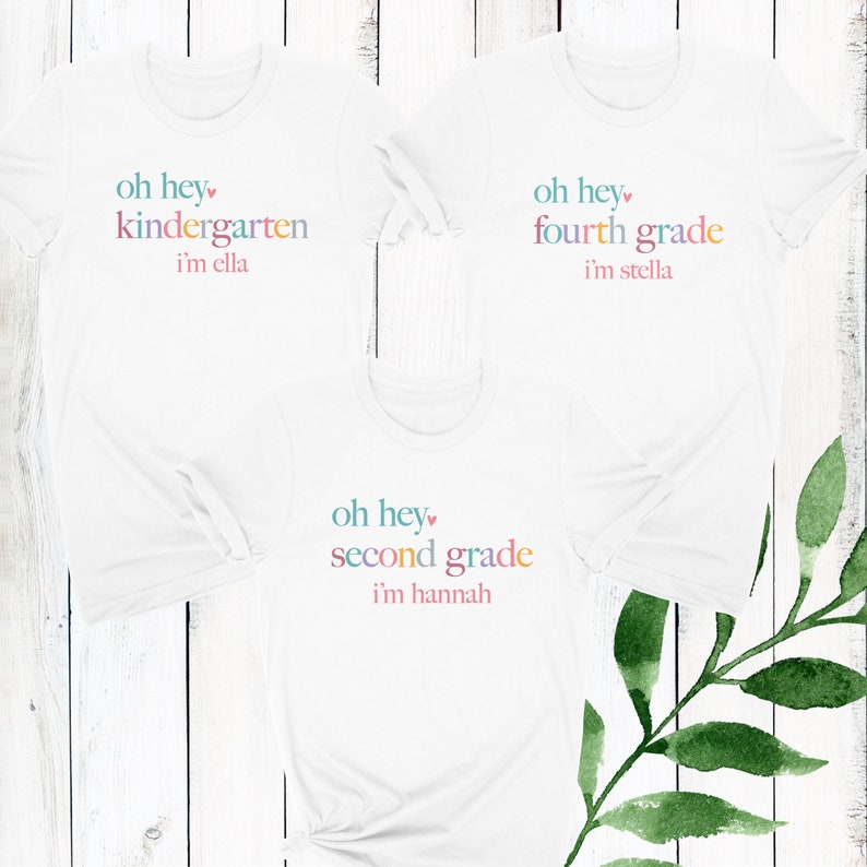 May include: Three white t-shirts with colorful text. The shirts say "oh hey kindergarten i'm ella", "oh hey fourth grade i'm stella", and "oh hey second grade i'm hannah".