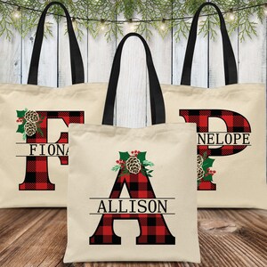 Pu&ograve; includere: Tre borse tote in tela personalizzate con manici neri. Ogni borsa presenta una grande lettera in tessuto scozzese rosso e nero con un design a pigna e agrifoglio. Le borse sono etichettate "Fiona", "Allison" e "Neloupe".