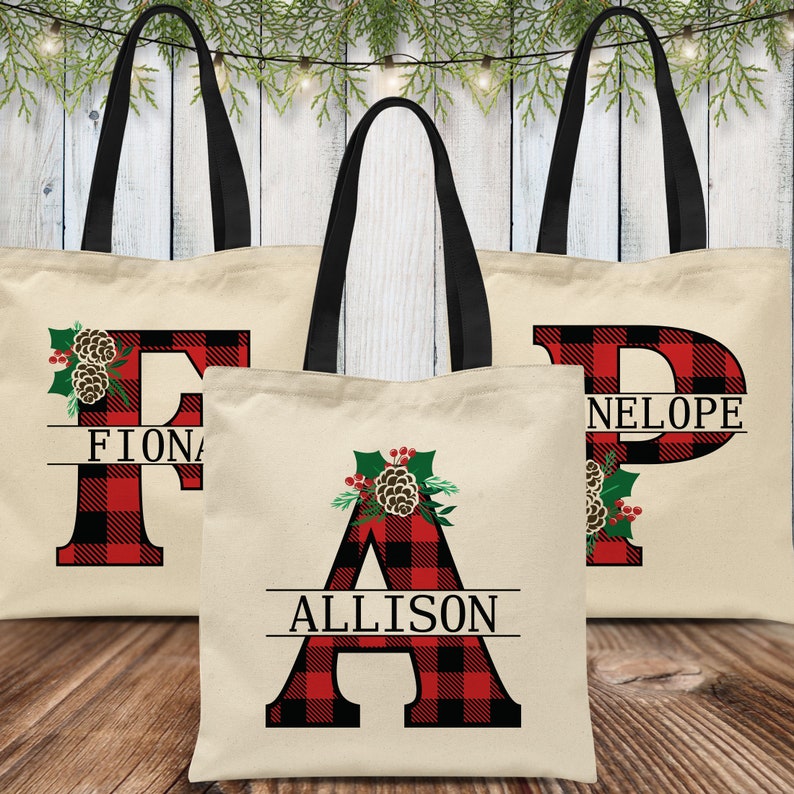 Pu&ograve; includere: Tre borse tote in tela personalizzate con manici neri. Ogni borsa presenta una grande lettera in tessuto scozzese rosso e nero con un design a pigna e agrifoglio. Le borse sono etichettate "Fiona", "Allison" e "Neloupe".