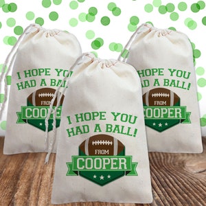 K&ouml;nnte beinhalten: Drei wei&szlig;e Kordelbeutel mit gr&uuml;nen und braunen Designs zum Thema Fu&szlig;ball. Die Beutel tragen den Text "Ich hoffe, du hattest Spa&szlig;!" und "Von Cooper".