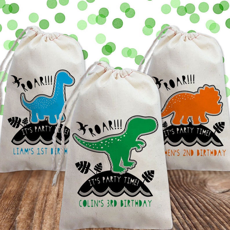 May include: Three white fabric gift bags with dinosaur designs and the text "ROAR!!! It's party time!"  The bags are personalized with the names Liam, Colin, and Hen and their ages.