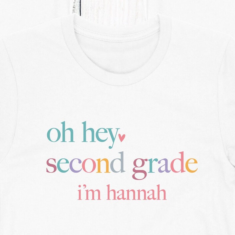 May include: White t-shirt with the text "oh hey" in teal, a pink heart, "second grade" in multicolored text, and "i'm hannah" in pink text.