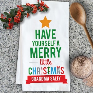 May include: White kitchen towel with a green Christmas tree design. The tree has a yellow star on top and the text "HAVE YOURSELF A MERRY little CHRISTMAS GRANDMA SALLY" in green, red, and white.
