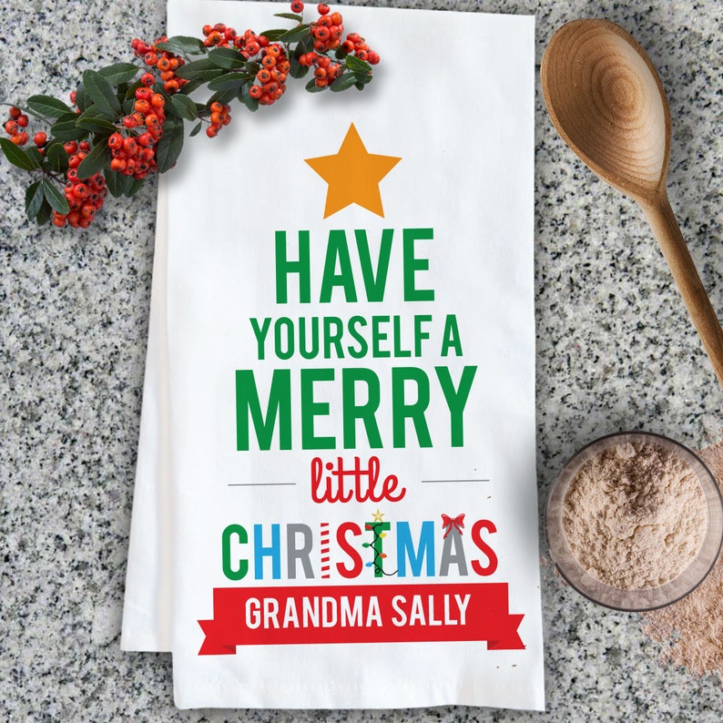 May include: White kitchen towel with a green Christmas tree design. The tree has a yellow star on top and the text "HAVE YOURSELF A MERRY little CHRISTMAS GRANDMA SALLY" in green, red, and white.