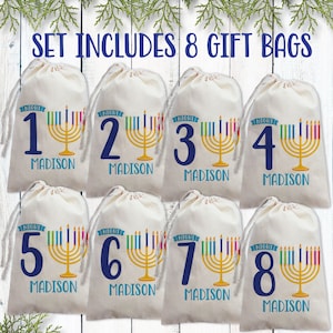 May include: Set of eight white gift bags with blue numbers 1 through 8 and the word "NIGHT" in a blue banner. Each bag features a gold menorah with rainbow-colored candles and the name "MADISON" printed below.