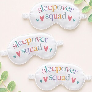 Puede incluir: Tres antifaces blancos con las palabras "sleepover squad" en letras coloridas y peque&ntilde;os corazones. Cada antifaz tiene una banda el&aacute;stica para un ajuste c&oacute;modo. Los antifaces est&aacute;n hechos de un material suave similar al sat&eacute;n.