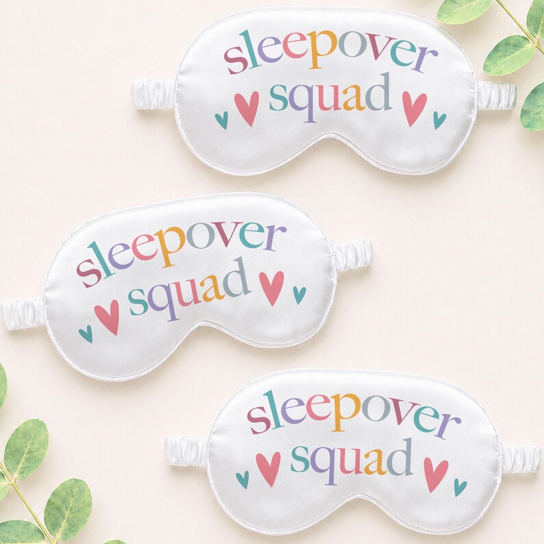 Puede incluir: Tres antifaces blancos con las palabras "sleepover squad" en letras coloridas y peque&ntilde;os corazones. Cada antifaz tiene una banda el&aacute;stica para un ajuste c&oacute;modo. Los antifaces est&aacute;n hechos de un material suave similar al sat&eacute;n.