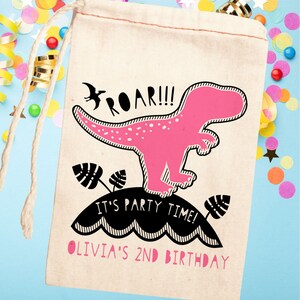 May include: A pink dinosaur with black outlines and white spots stands on a black and white striped hill with the text "Roar!!! It's party time! Olivia's 2nd Birthday" printed on the hill. The dinosaur is on a white canvas bag with a drawstring.