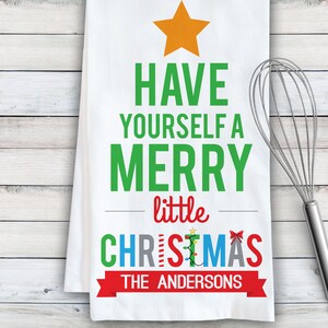 May include: White kitchen towel with a green Christmas tree design. The tree has a star on top and the text "Have yourself a merry little Christmas" with the name "The Andersons" at the bottom.