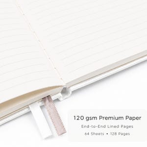 May include: An open notebook with cream-colored lined pages, featuring a white ribbon bookmark and a light brown ribbon bookmark. Text on the image reads: 120 gsm Premium Paper, End-to-End Lined Pages, 64 Sheets, 128 Pages.