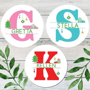 May include: Three round Christmas ornaments with a white background and a large letter in the center. The letters are G, S, and K. Each letter is a different color: pink, blue, and red. Each ornament has a Christmas tree, a star, and a gift box on the top and bottom of the letter. The names "Gret
