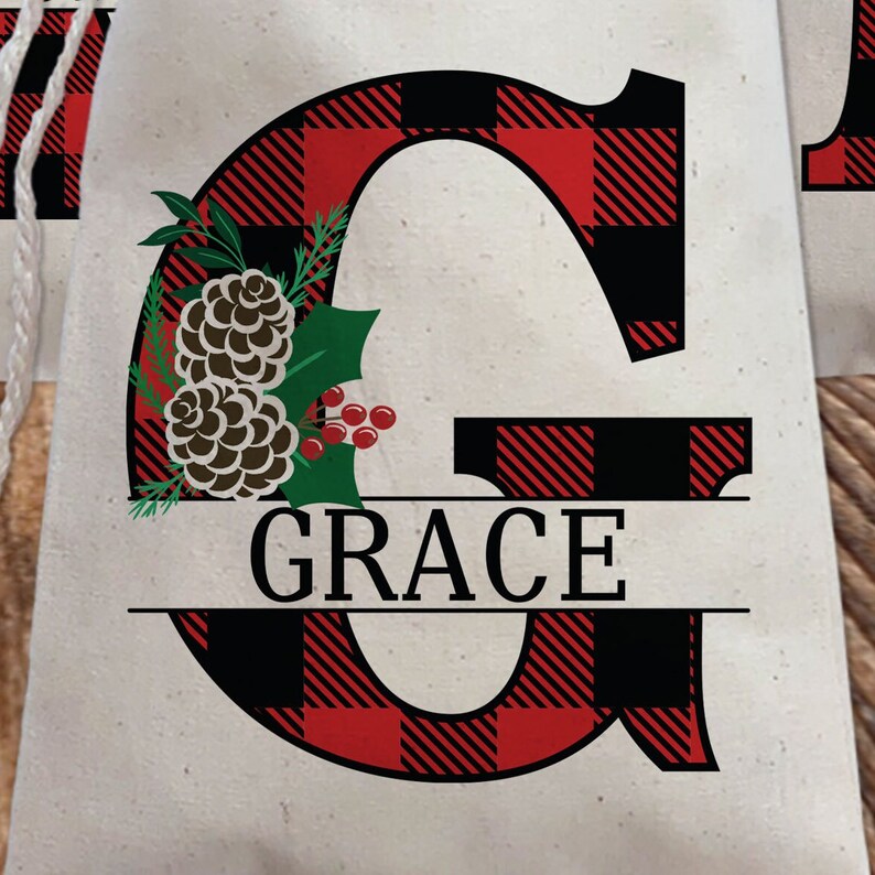 Pu&ograve; includere: Una lettera G in tessuto a quadri rosso e nero con un motivo di pigna e ramo di agrifoglio. Il nome "GRACE" &egrave; scritto in lettere nere sotto la lettera.