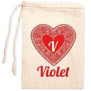 May include: A white cotton drawstring bag with a red heart design. The heart has a lace pattern and a white letter "V" in the center. The word "Violet" is written in red below the heart.