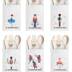 May include: White paper cutlery holders with gold-colored utensils. Each holder features a different watercolor illustration of characters from The Nutcracker ballet, including a ballerina, a nutcracker, and toy soldiers. The text "THE HENDERSON FAMILY" is printed on each holder.