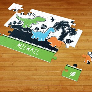 May include: A jigsaw puzzle featuring a green dinosaur, a blue dinosaur, and an orange dinosaur with palm trees and the text ROAR!!! and MICHAEL. The puzzle pieces are white, green, blue, orange, and black with a graphic illustration of prehistoric life.
