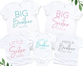 May include: Set of four white t-shirts with different sibling titles and names. The shirts read "Big Brother Oliver", "Big Sister Stella", "Little Sister Isabel", and "Middle Brother Greyson".