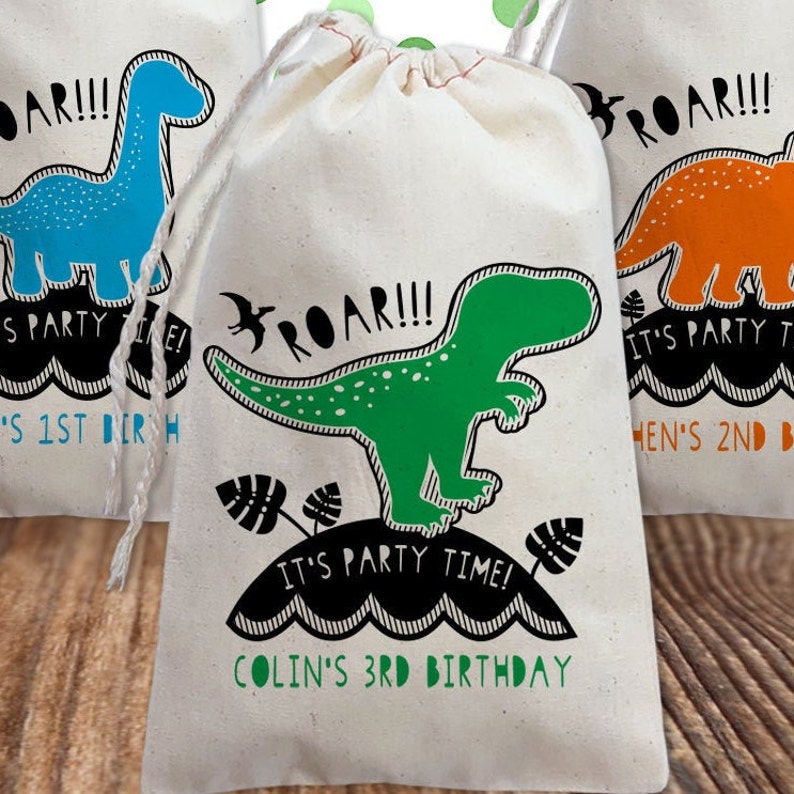 May include: A white canvas drawstring bag with a green dinosaur graphic and the text "ROAR!!! It's party time! Colin's 3rd Birthday".