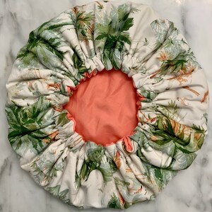 May include: A white and green patterned hair bonnet with a tropical design. The interior is a solid peach color. The bonnet is gathered at the edge with an elastic band.