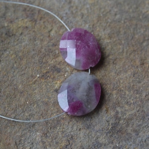 May include: Two round, faceted gemstone beads with a pink and white color pattern. The beads are strung on a clear thread.