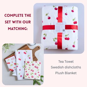 May include: A white plush blanket wrapped in a red ribbon, a white tea towel with a red cherry pattern, and a square Swedish dishcloth with a matching cherry print. The text reads: COMPLETE THE SET WITH OUR MATCHING: Tea Towel, Swedish dishcloths, Plush Blanket.