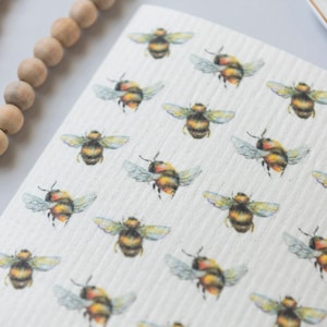 May include: A white ceramic mug with a black handle and the text "But First, Coffee" in a bold, black font. The mug is set against a blurred background, suggesting a cozy setting.