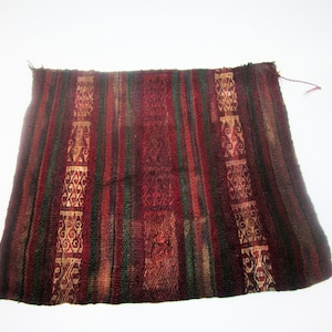 Puede incluir: Textil tejido rectangular con un patrón de rayas en rojo, verde y dorado. El textil presenta patrones geométricos decorativos y parece hecho a mano. Los bordes están deshilachados, lo que sugiere edad o desgaste. Podría ser un objeto histórico.