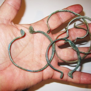 Könnte beinhalten: Eine Sammlung von fünf antiken Bronzearmbändern, jedes mit einer leicht unterschiedlichen Form und Patina. Die Armbänder sind in einem Stapel angeordnet und zeigen ihre komplizierten Details.