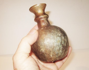 Könnte beinhalten: Eine kleine, runde, braune Glasflasche mit einem schmalen Hals und einer ausgestellten Öffnung. Die Flasche hat ein abgenutztes, altes Aussehen.