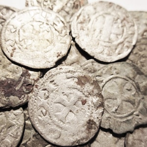 Puede incluir: Un conjunto de monedas antiguas de plata, cada una con intrincados diseños en relieve. Las monedas muestran signos de edad y desgaste, con detalles visibles de cruces y otros símbolos. El color general es plateado apagado con zonas más oscuras.