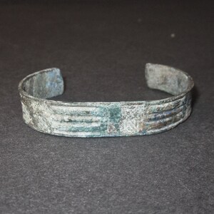Könnte beinhalten: Ein silberfarbenes Metallarmband mit einem dekorativen Design. Das Armband hat einen abgenutzten, gealterten Look mit einer grünen Patina.