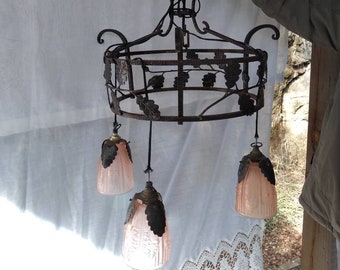 May include: A wrought iron chandelier with a circular frame decorated with leaf designs. The chandelier has three pink glass shades with leaf accents.