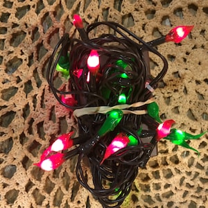 May include: A string of Christmas lights with red and green bulbs shaped like chili peppers. The lights are tangled together and are ready to be hung.
