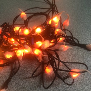 May include: A string of orange fairy lights with a warm glow. The lights are shaped like teardrops and are strung on a black wire.