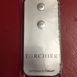 May include: A silver remote control with two buttons labeled "ON" and "OFF". The remote control has the text "TORCHIER" and "Technology by Liown" printed on it.
