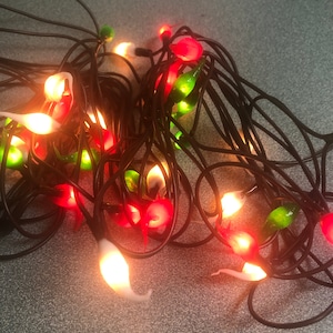 May include: A string of Christmas lights with red, green, and white bulbs. The lights are shaped like teardrops and are strung on a black wire.