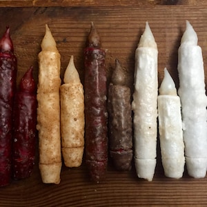 May include: A collection of ten decorative candles in various colors, including red, brown, white, and beige. The candles are all different sizes and have a textured, rustic look.