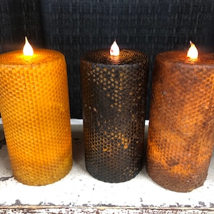 May include: Three pillar candles with a honeycomb design. The candles are lit and are in the colors yellow, brown, and black.